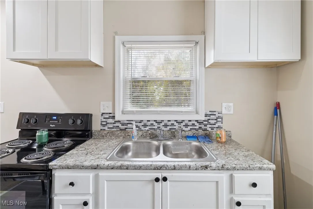 Kitchen with black range with electric stovetop, white cabinets, and light countertops