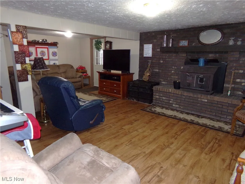 Living area with a wood stove, a textured ceiling, and wood finished floors