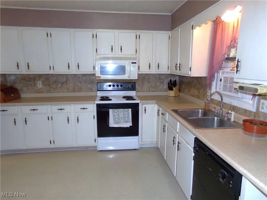 Kitchen featuring electric range, light countertops, white microwave, and white cabinets