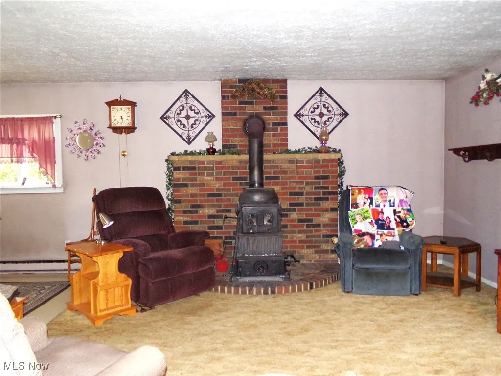 Carpeted living area with a wood stove, a textured ceiling, and a baseboard heating unit