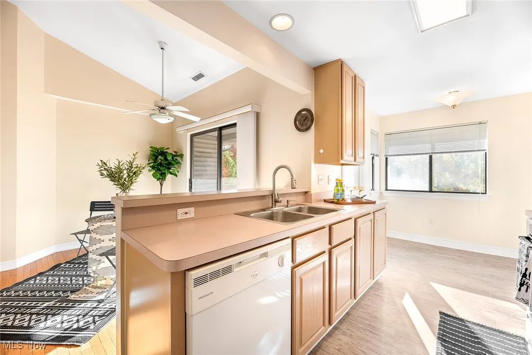 Kitchen featuring white dishwasher, light brown cabinetry, light wood-style floors, and light countertops