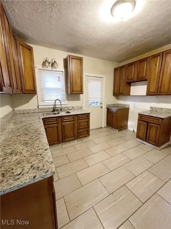 Kitchen with brown cabinets, a textured ceiling, and light stone countertops