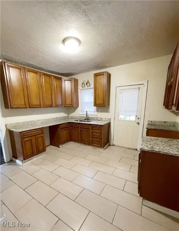 Kitchen with brown cabinetry, a textured ceiling, and light stone counters