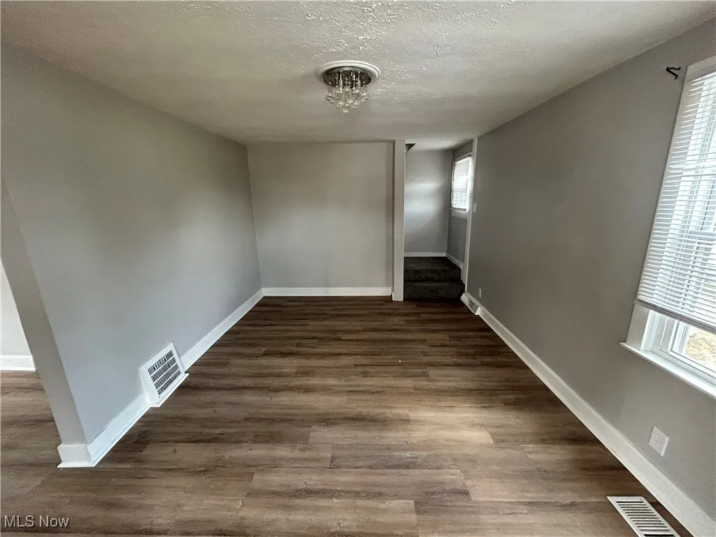 Spare room with a textured ceiling, dark wood-style flooring, and stairs