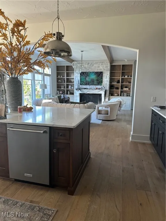 Kitchen with light wood finished floors, built in shelves, dark brown cabinets, dishwasher, and light stone counters
