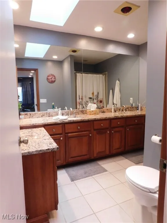 Full bathroom with light tile patterned flooring, double vanity, a shower with curtain, a skylight, and recessed lighting