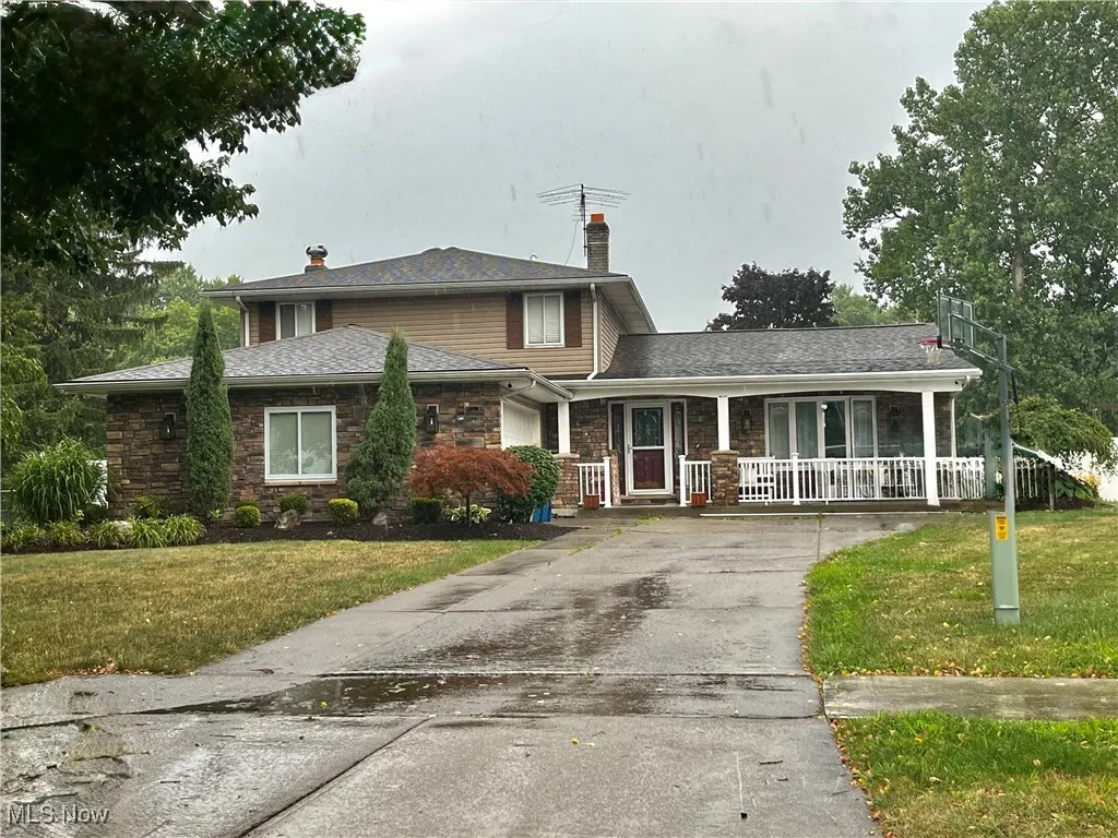View of front facade featuring a chimney, stone siding, a front yard, and covered porch