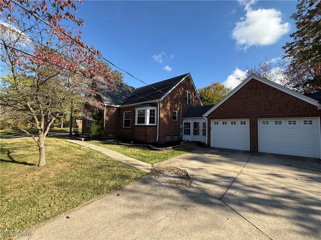 View of side of home with brick siding, driveway, a lawn, and an attached garage