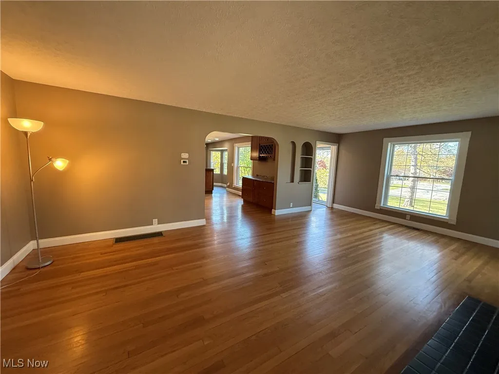 Unfurnished living room featuring arched walkways, light wood-style flooring, and a textured ceiling