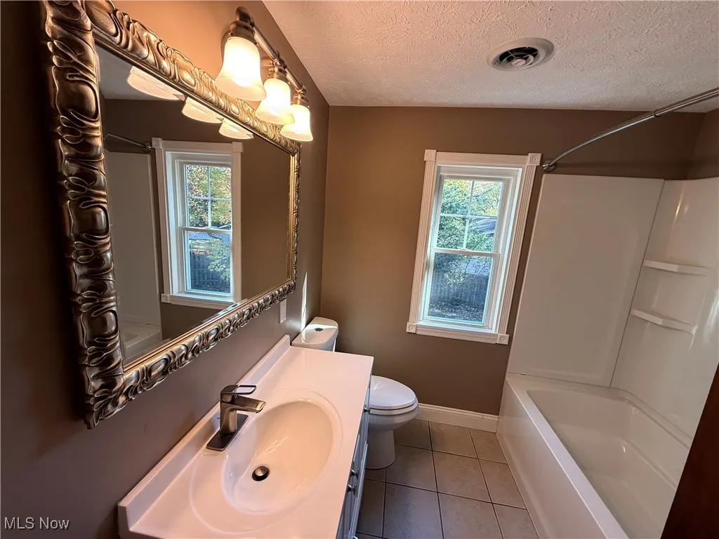 Full bath featuring a textured ceiling, light tile patterned floors, vanity, and tub / shower combination