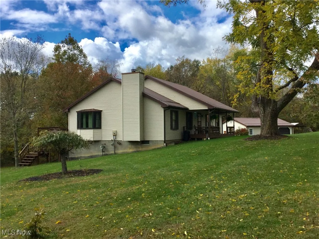 View of side of home featuring a wooden deck, a yard, a chimney, and view of wooded area