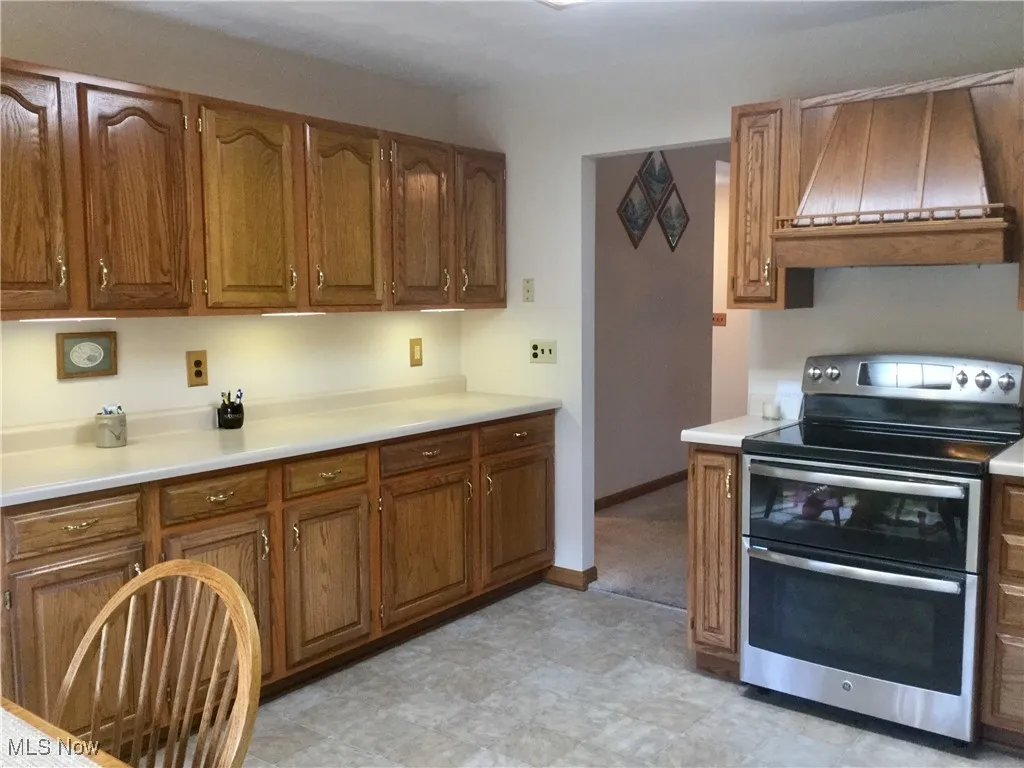 Kitchen with oven range, light countertops, brown cabinetry, and premium range hood