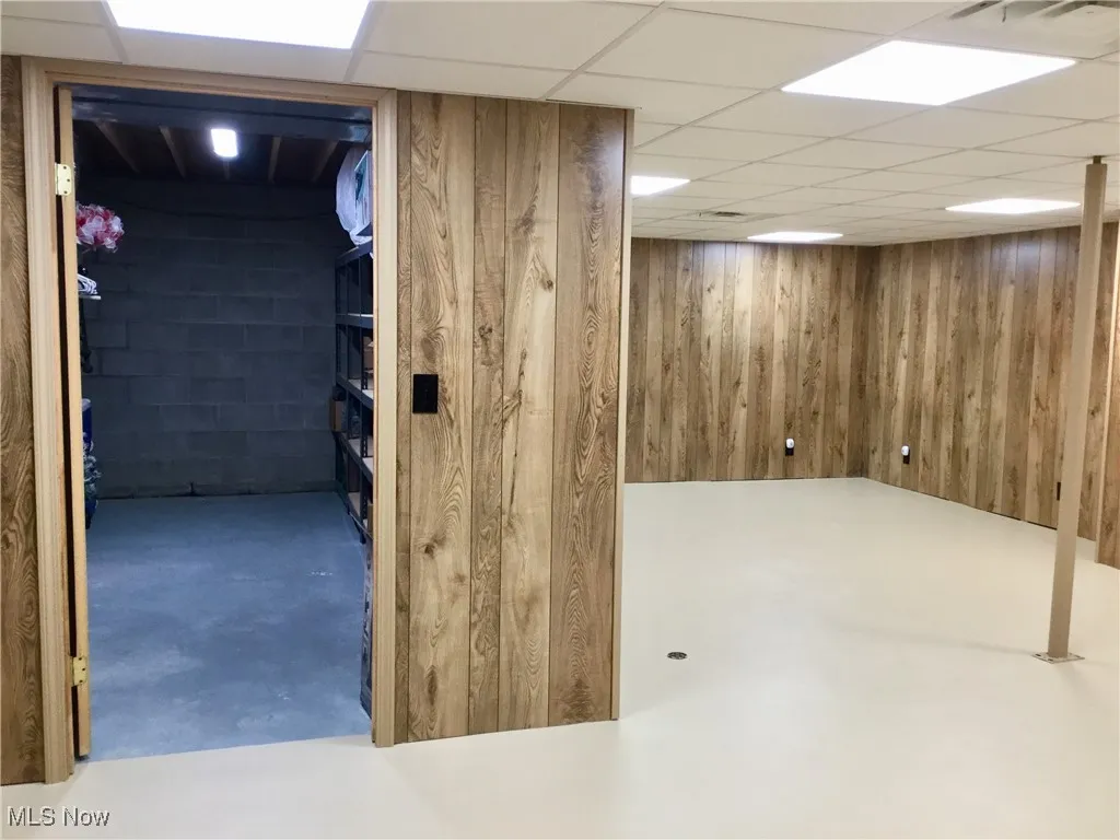 Finished basement featuring a drop ceiling and wood walls