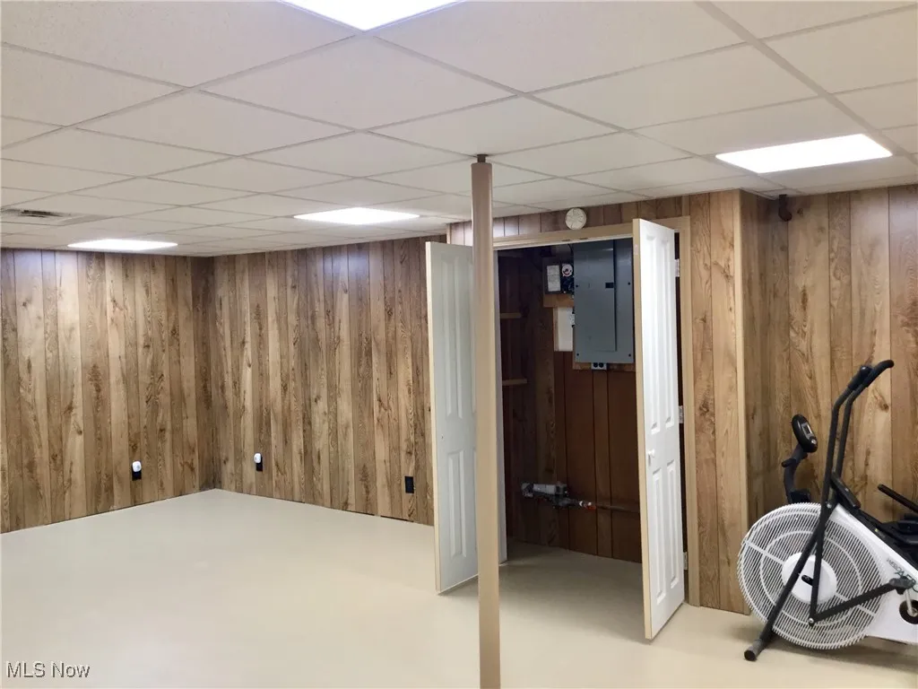 Finished below grade area with wood walls, a paneled ceiling, and electric panel