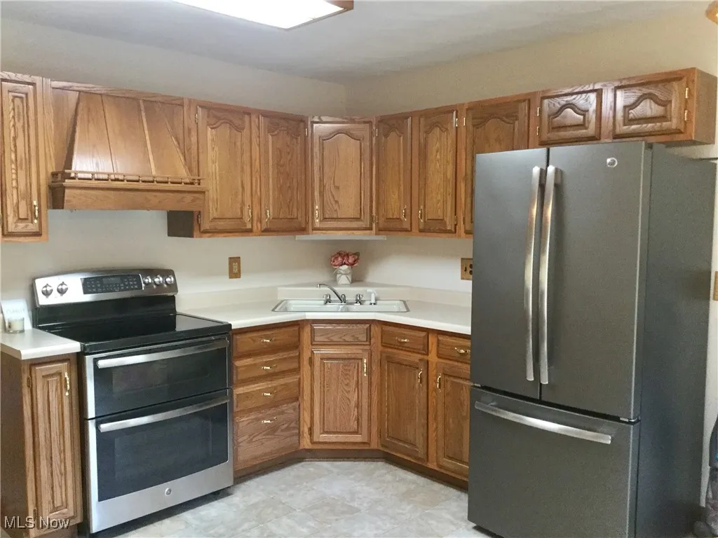Kitchen with appliances with stainless steel finishes, premium range hood, brown cabinetry, and light countertops