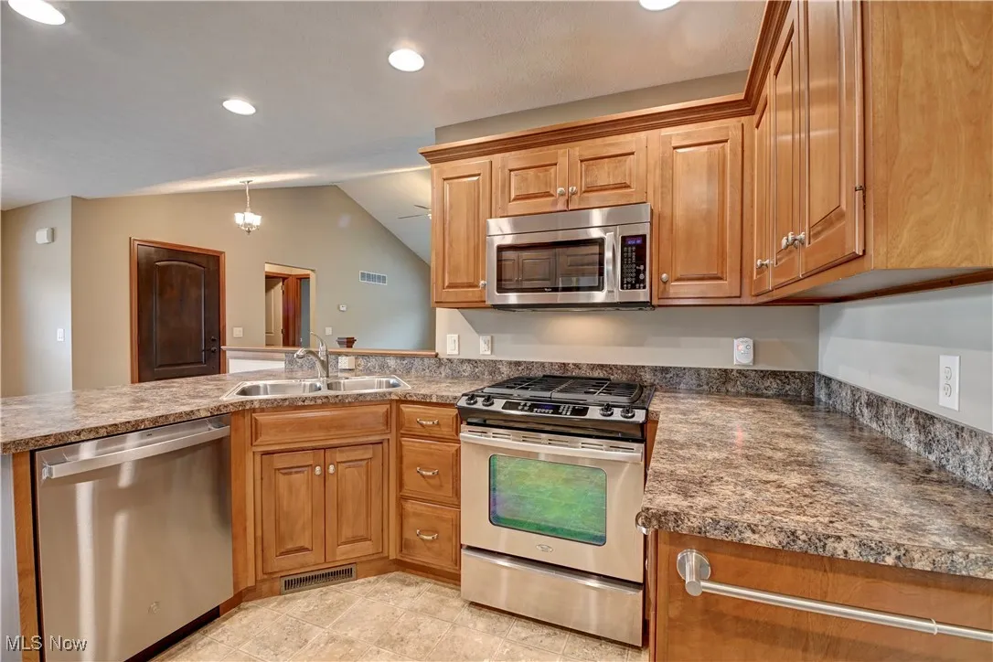 Kitchen with stainless steel appliances, brown cabinets, vaulted ceiling, recessed lighting, and decorative light fixtures