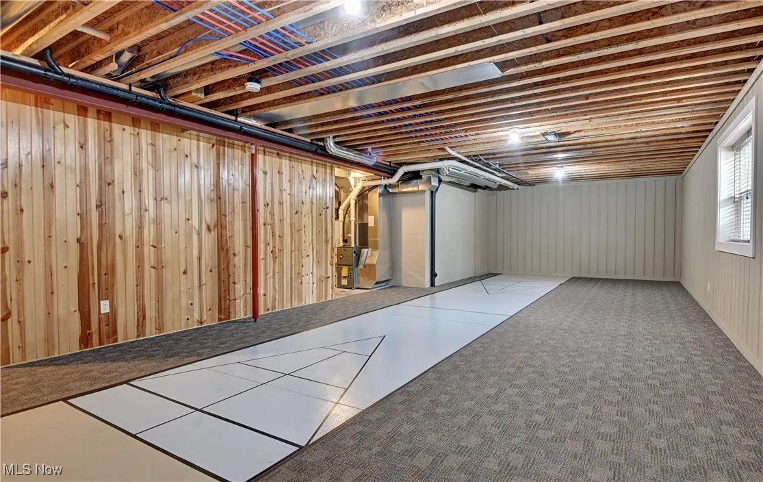 Basement featuring wooden walls, heating unit, tile patterned flooring, and carpet floors