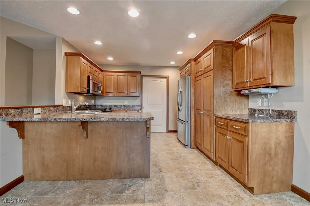 Kitchen with brown cabinets, a peninsula, a kitchen breakfast bar, appliances with stainless steel finishes, and recessed lighting