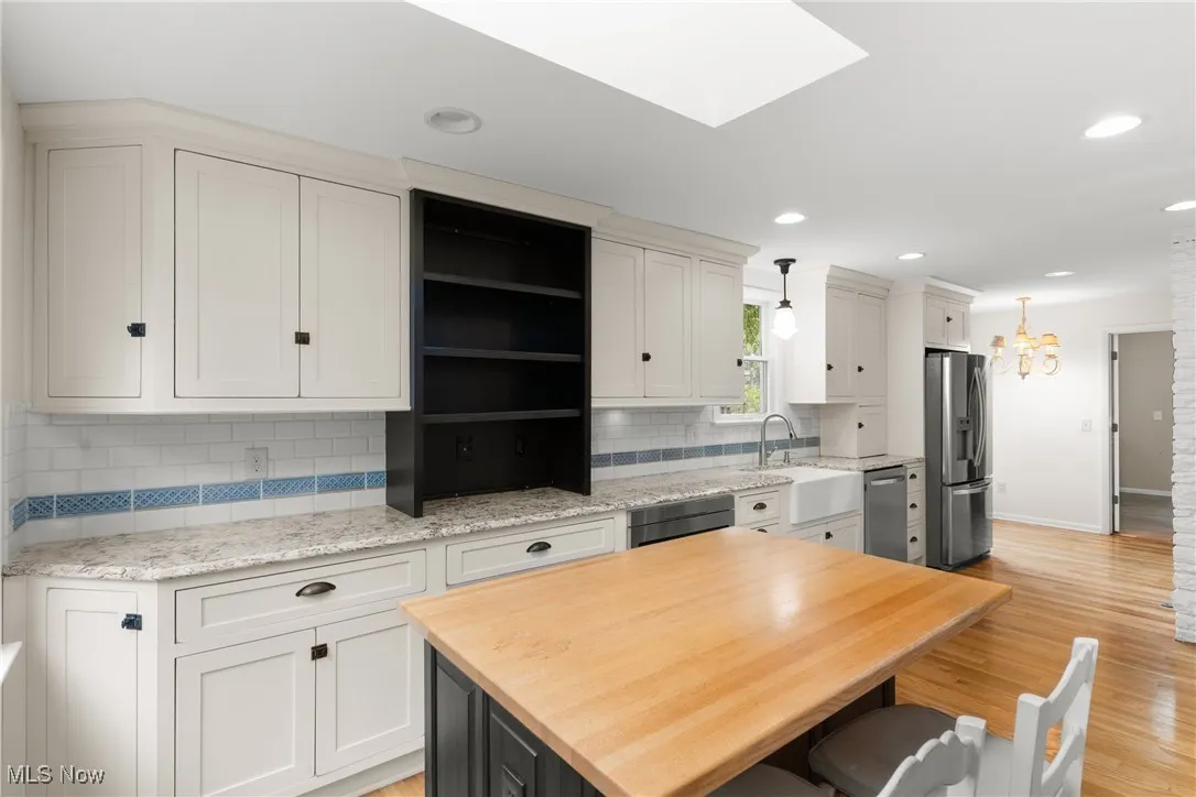 Kitchen with a skylight, light stone counters, pendant lighting, light wood-style floors, and white cabinets