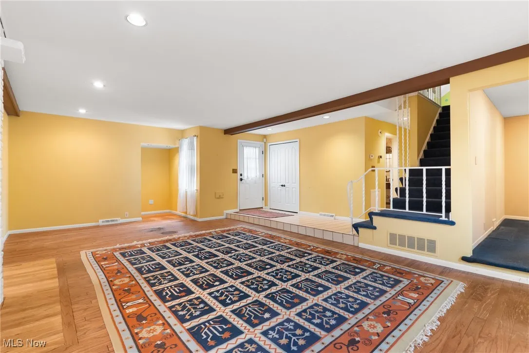 Unfurnished living room featuring recessed lighting, light wood finished floors, stairway, and beam ceiling
