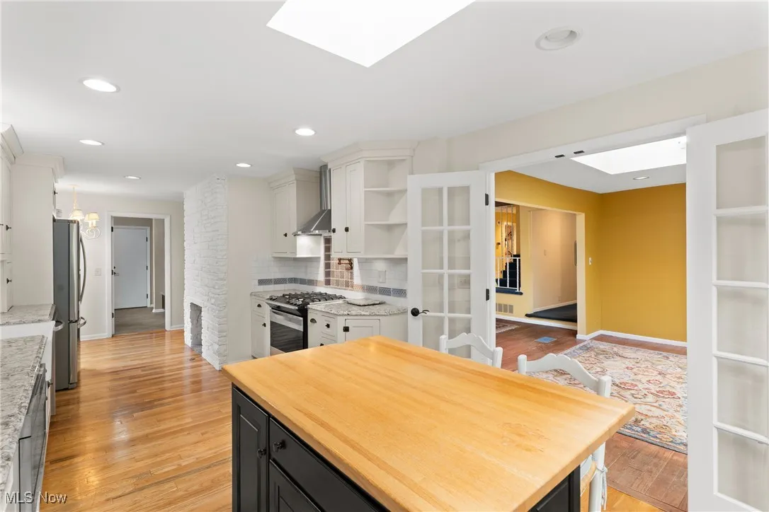 Kitchen with light wood-type flooring, a skylight, open shelves, white cabinets, and stainless steel appliances