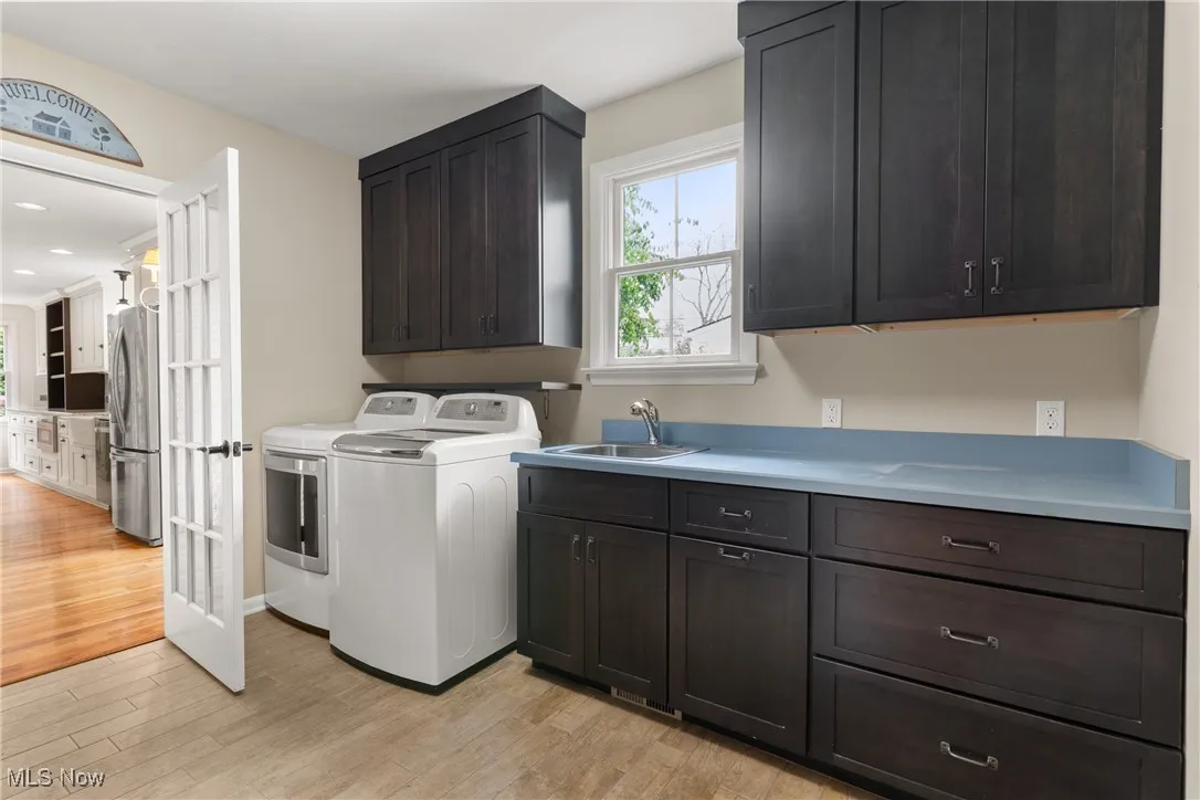 Washroom with light wood-type flooring, washing machine and clothes dryer, and cabinet space