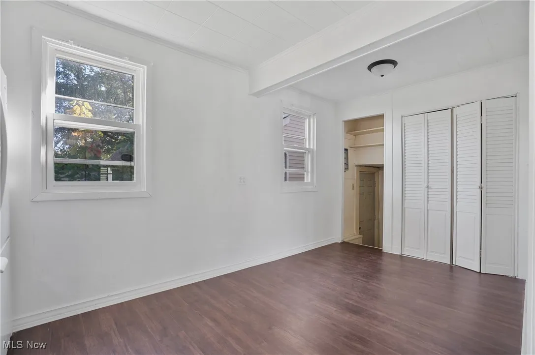 Unfurnished bedroom featuring crown molding, dark wood-style flooring, a closet, and beamed ceiling