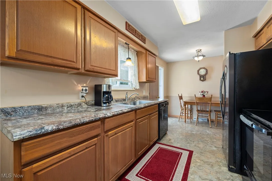 Kitchen with brown cabinetry, black appliances, stone finish flooring, and hanging light fixtures