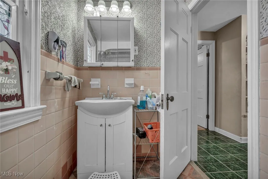 Bathroom featuring vanity, wallpapered walls, wainscoting, tile walls, and tile patterned flooring