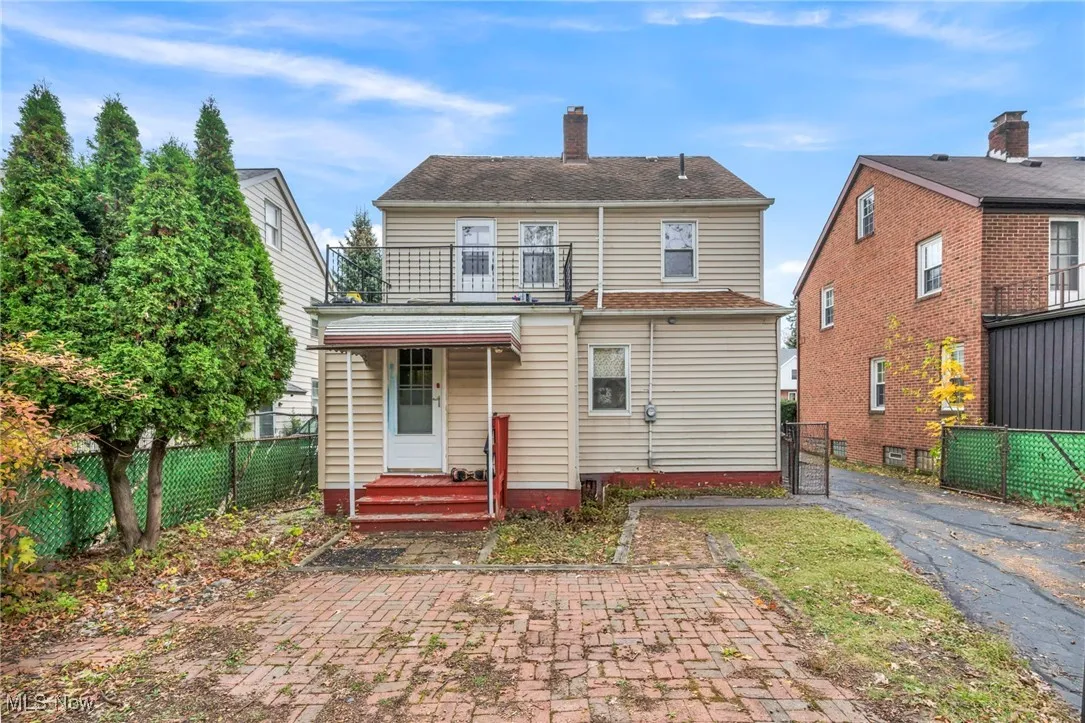 Rear view of house featuring a chimney, a balcony, and a gate