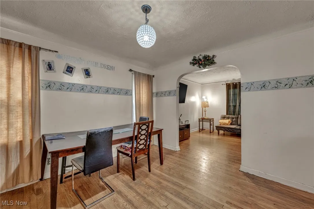 Dining room featuring arched walkways, light wood finished floors, a textured ceiling, and an office area
