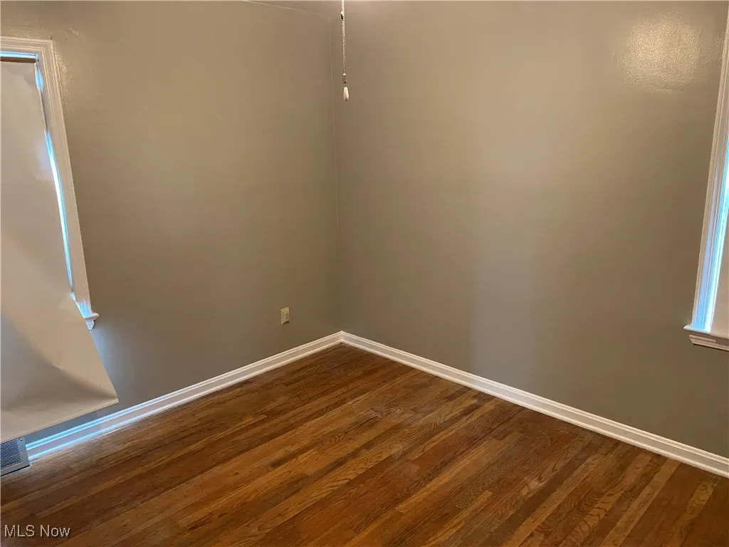 Spare room with dark wood-type flooring and baseboards