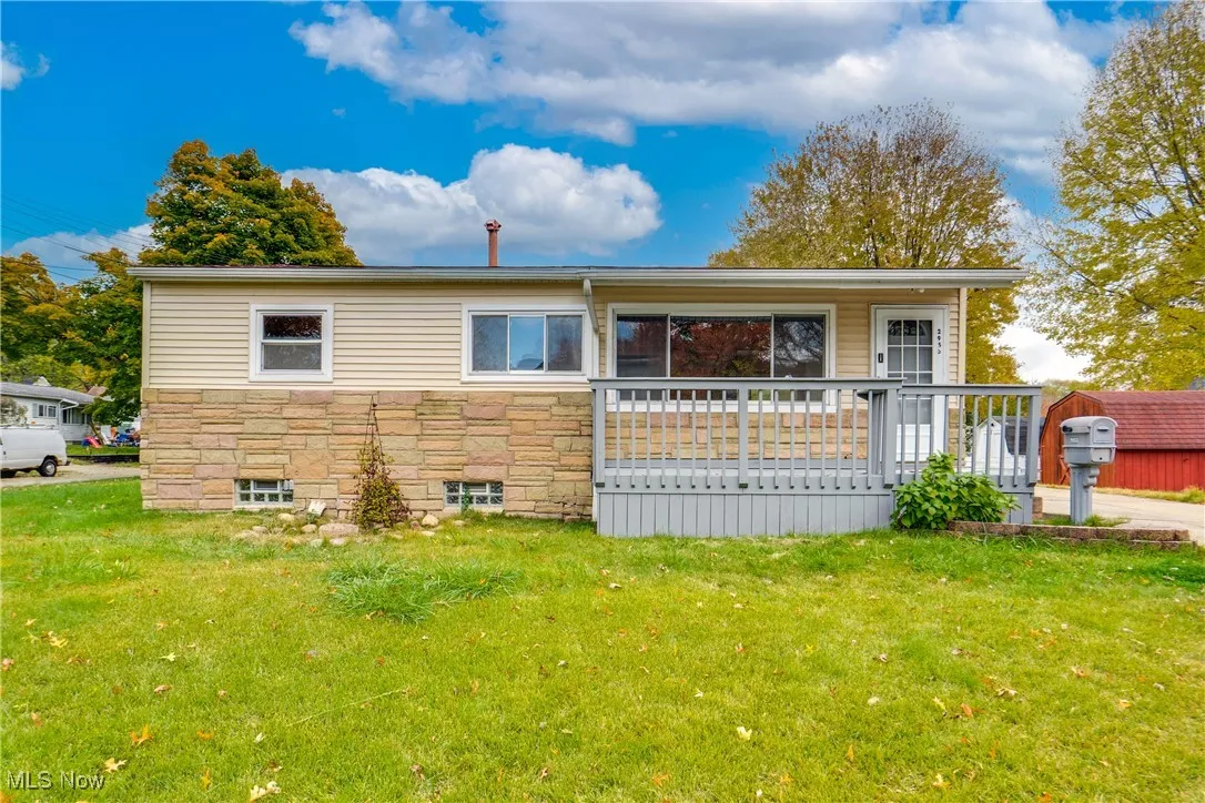 View of front facade with stone siding, a front yard, a deck, and heating fuel