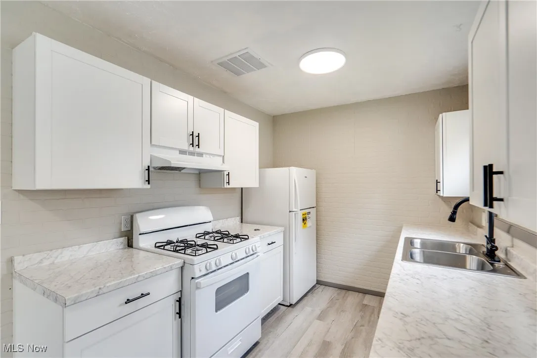 Kitchen with white appliances, light wood-type flooring, light countertops, white cabinetry, and under cabinet range hood