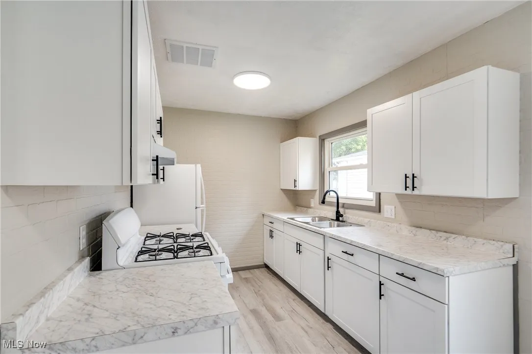 Kitchen with white appliances, light countertops, white cabinets, and light wood-style flooring