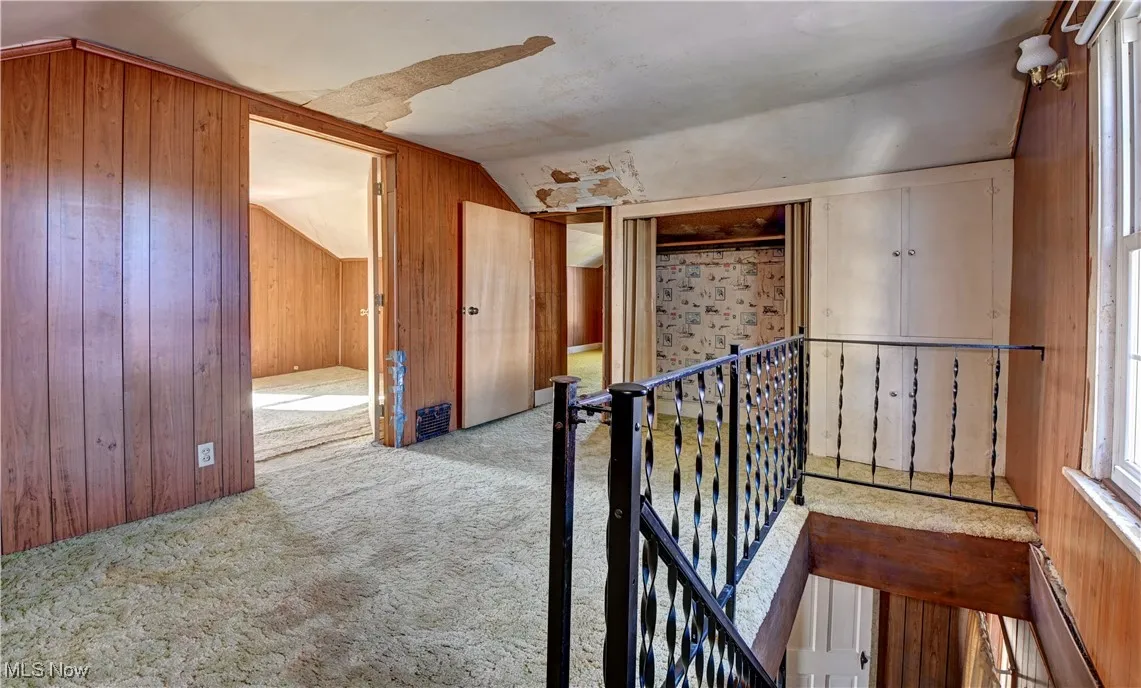 Hall with wood walls, lofted ceiling, a baseboard heating unit, carpet floors, and an upstairs landing