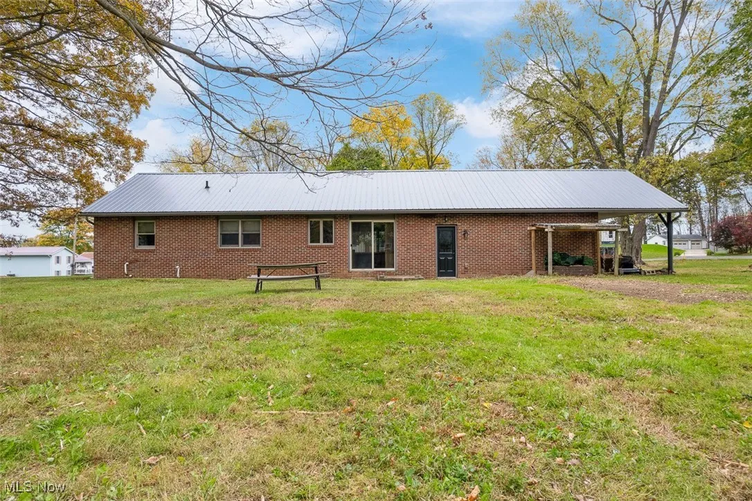 Rear view of house featuring a lawn, a metal roof, and brick siding