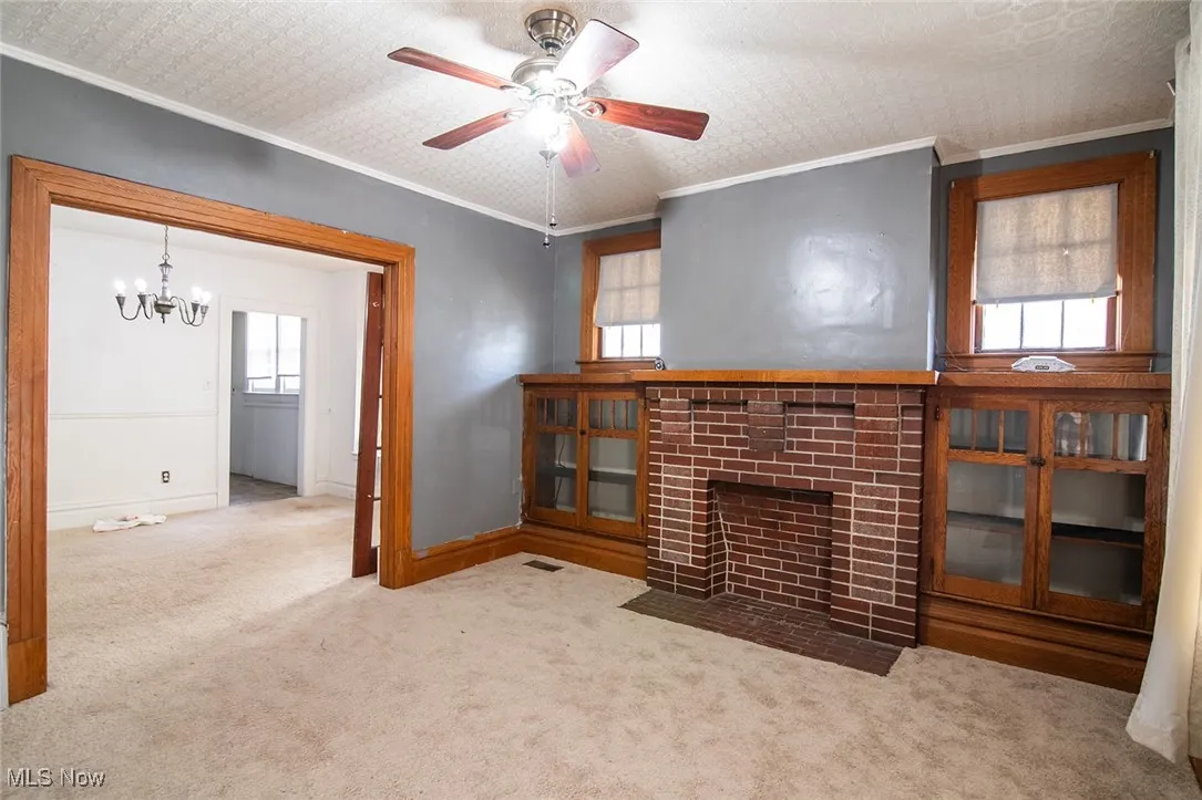 Unfurnished living room with ornamental molding, carpet flooring, a fireplace, a ceiling fan, and a chandelier
