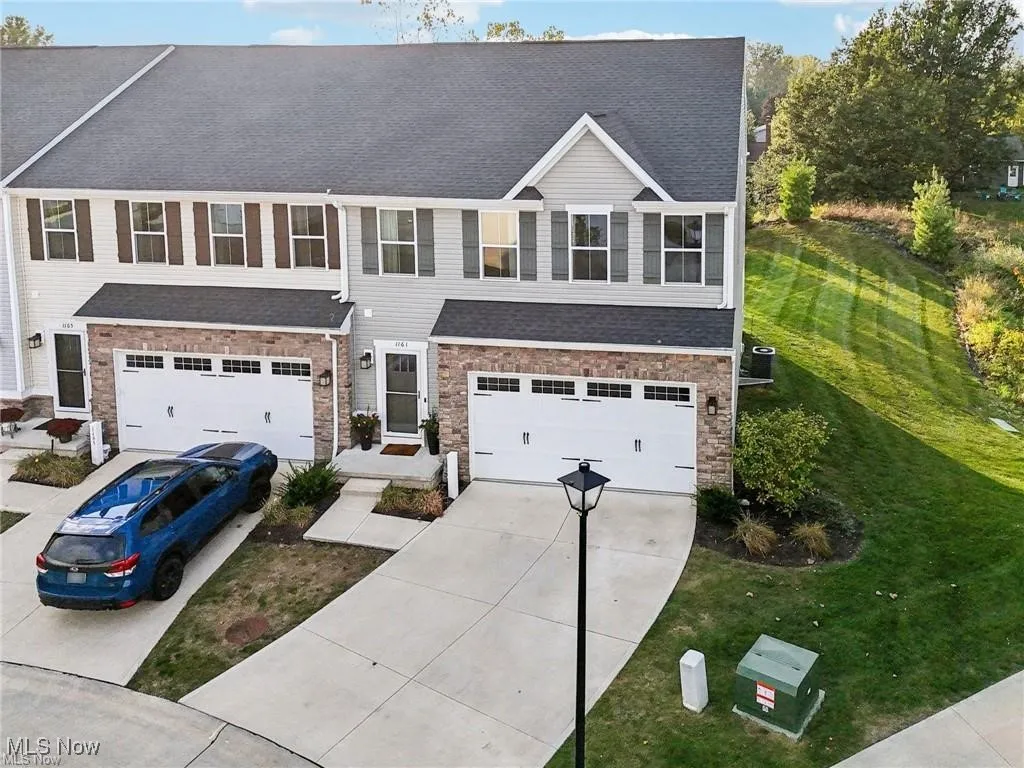 View of front of property with driveway, stone siding, an attached garage, and roof with shingles