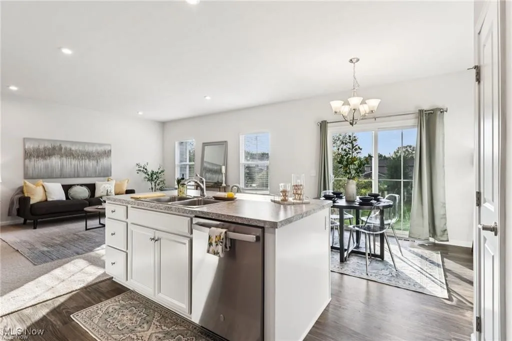 Kitchen with white cabinetry, dishwasher, open floor plan, dark wood finished floors, and decorative light fixtures