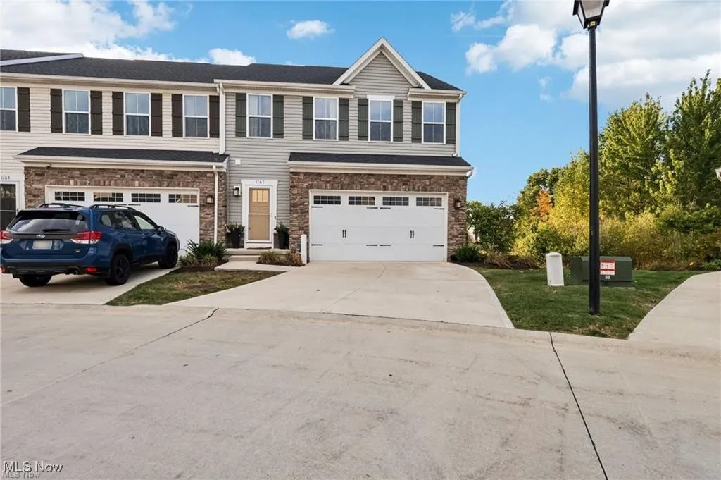 View of front of property featuring driveway, stone siding, an attached garage, and a front lawn