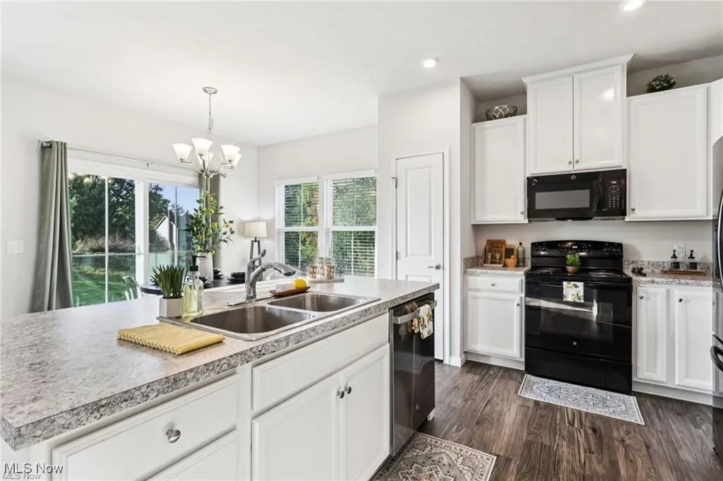 Kitchen with black appliances, white cabinets, light countertops, dark wood-type flooring, and recessed lighting