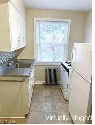 Kitchen featuring stainless steel countertops, white appliances, radiator heating unit, white cabinets, and decorative backsplash