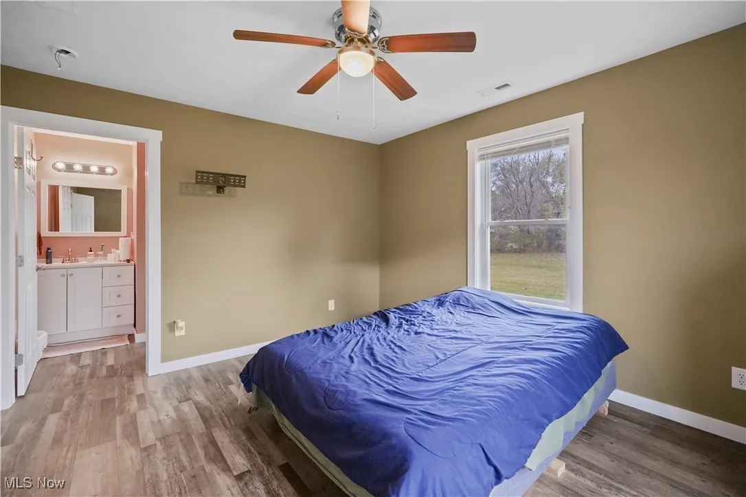 Bedroom with wood finished floors, ceiling fan, and ensuite bathroom