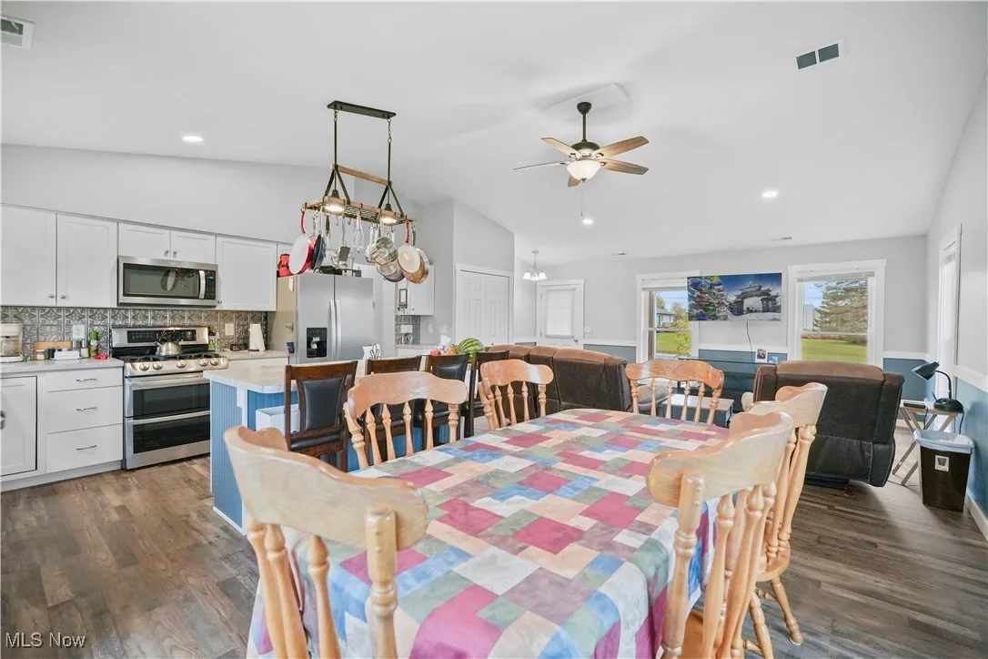 Dining room with vaulted ceiling, dark wood finished floors, ceiling fan, recessed lighting, and a chandelier
