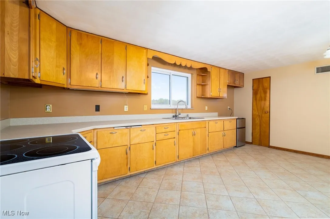 Kitchen featuring white electric range, light countertops, freestanding refrigerator, light tile patterned flooring, and open shelves