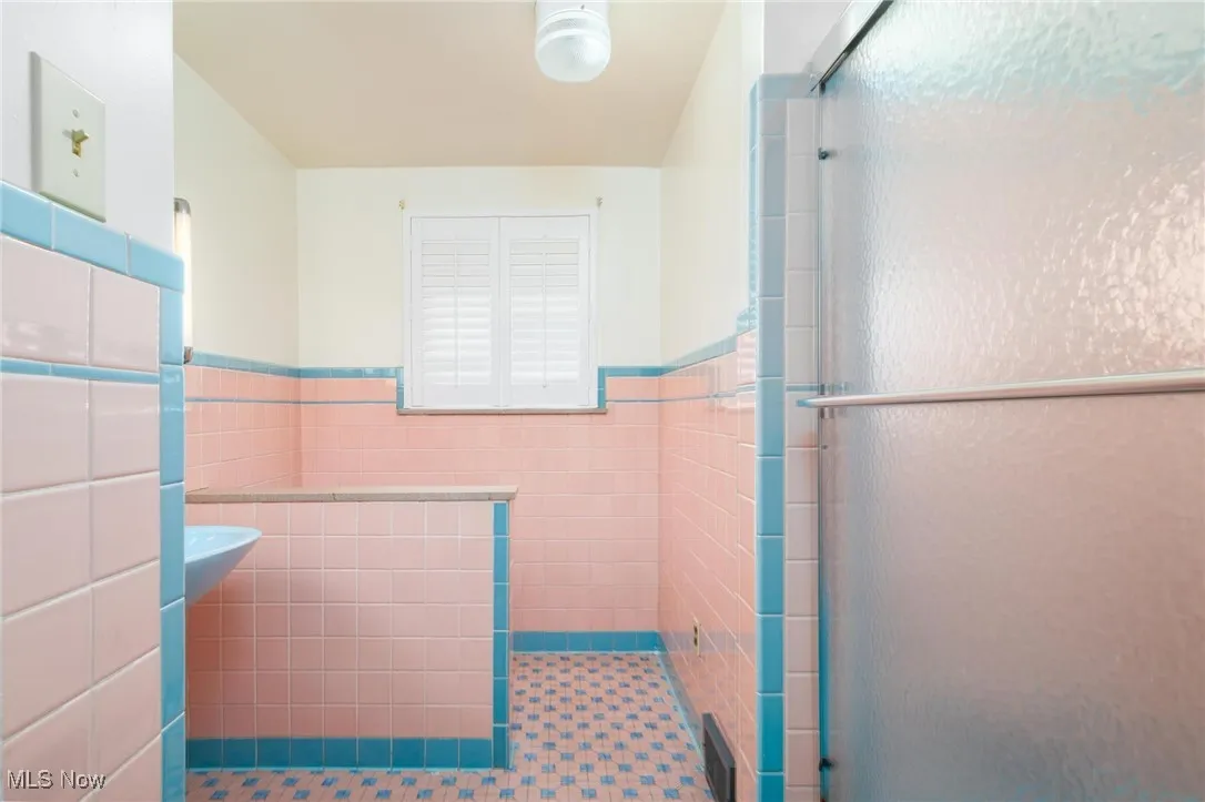 Full bathroom featuring tile walls, a wainscoted wall, a stall shower, and tile patterned floors