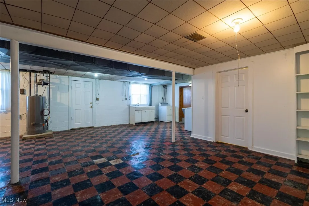 Basement featuring dark floors, concrete block wall, water heater, and a drop ceiling
