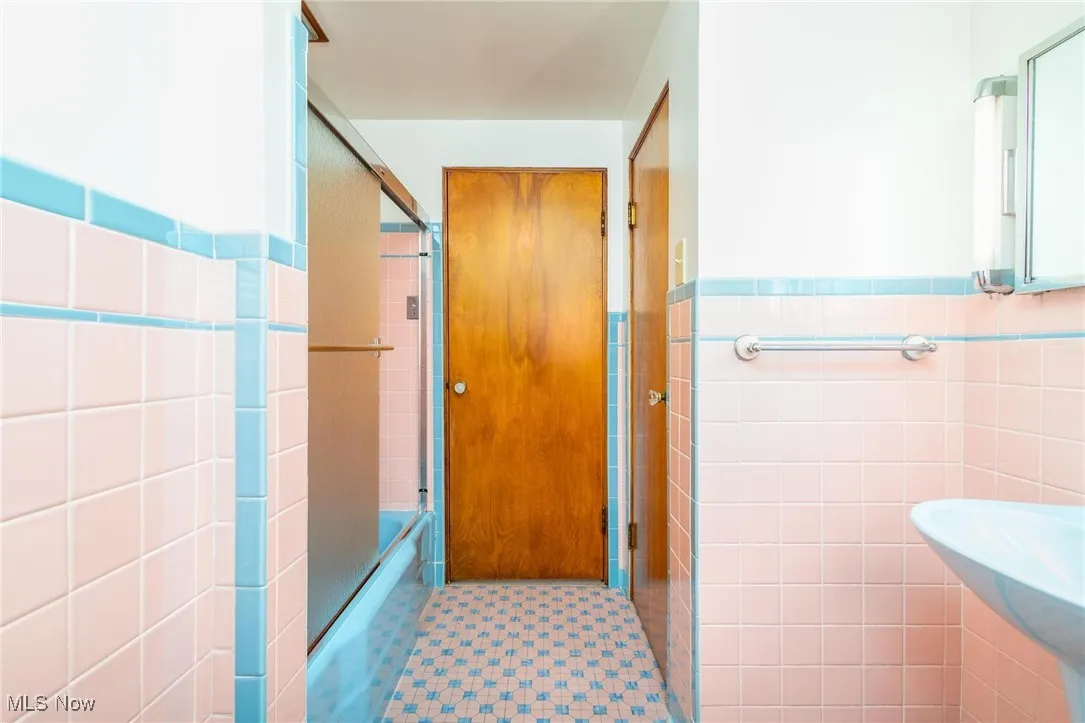 Full bathroom featuring tile walls, bath / shower combo with glass door, a wainscoted wall, and light tile patterned floors