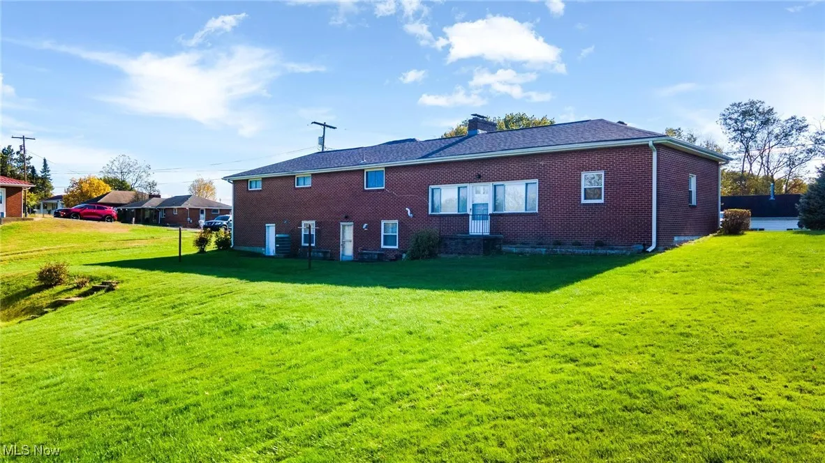 Back of house with a yard, a chimney, and brick siding